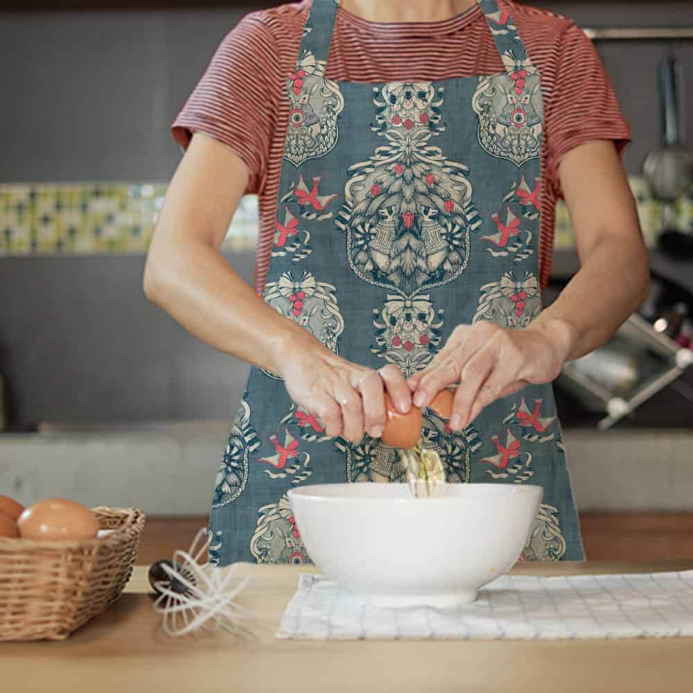 Christmas toile de jouy pattern shown in a mockup of an apron on a woman baking in the kitchen.