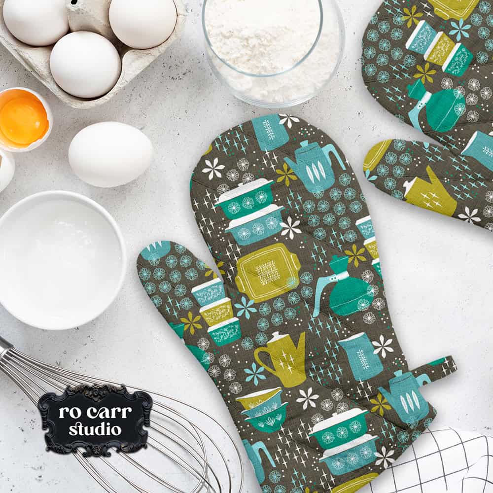Baking scene with eggs, milk and wisk, displaying a pair of oven mitts made of the pattern in teal.