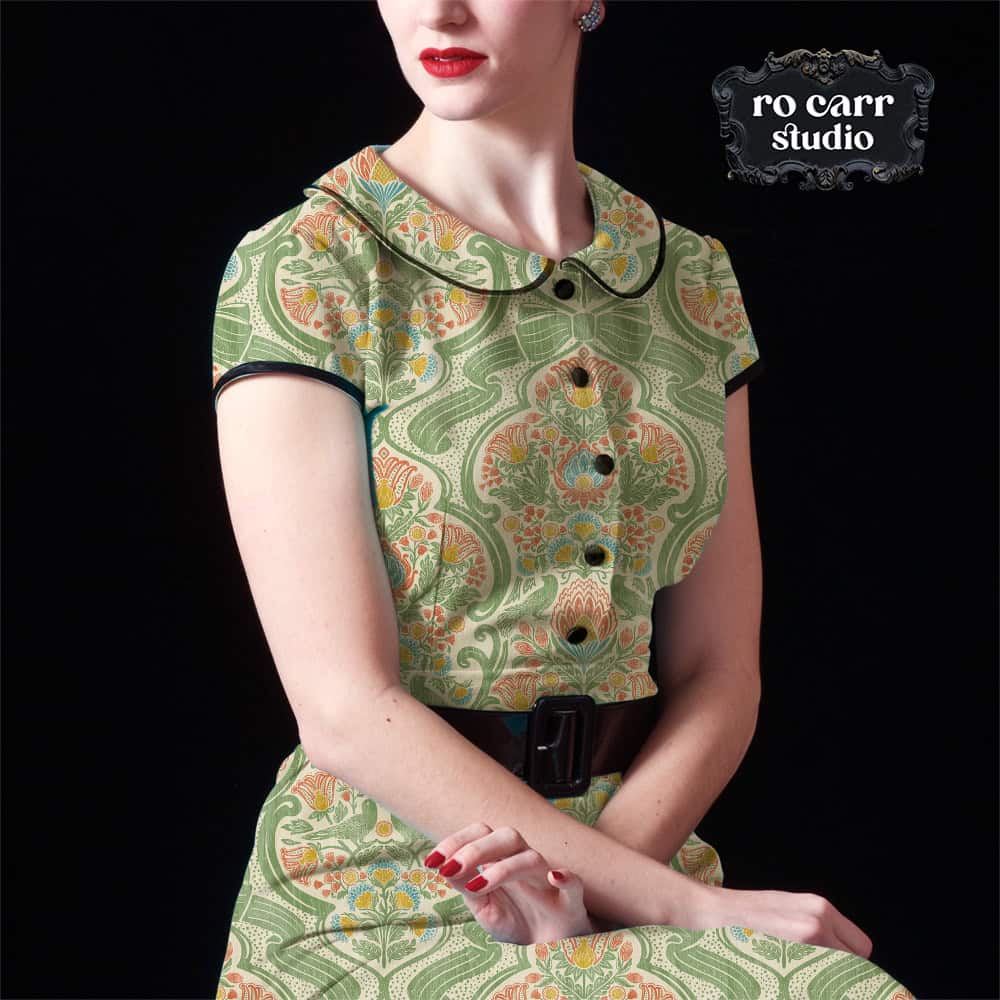 Model in a fitted Peter Pan collar dress in botanical chintz print, seated against a dark background.