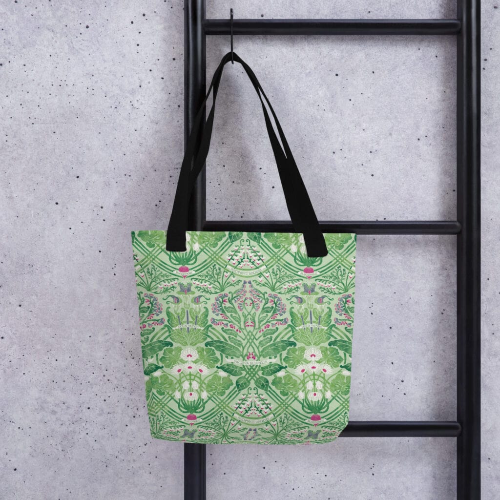 Tote bag with black straps hanging from a peg on a ladder, printed with vibrant green pattern, Rennie's Field Journal.