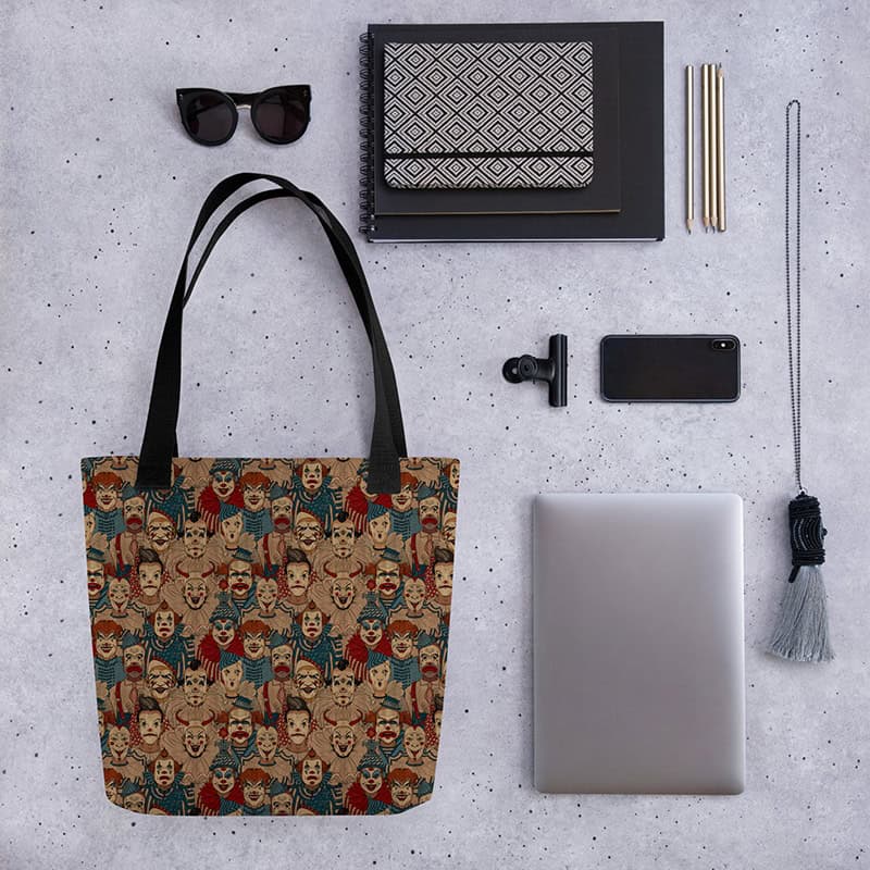 Creepy Circus Tote styled flat lay with sunglasses, notebook, phone, and laptop.