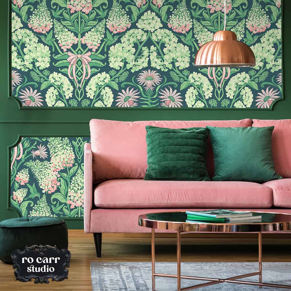 Pink sofa with green velvet pillows in front of hydrangea damask wallpaper, dark green wainscoting below, copper pendant light above.