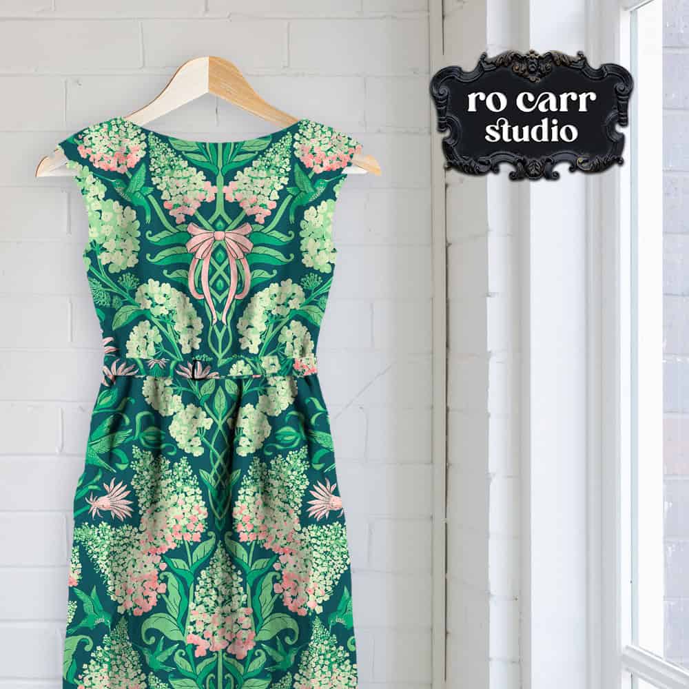 Sleeveless hydrangea-print sundress with a pink bow detail, hanging against a white wall.
