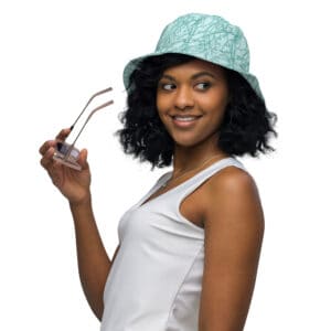 Model wearing the reversible bucket hat printed with Toile de Vie in aqua on one side, and a coordinating grosgrain striped pattern on the opposite side.