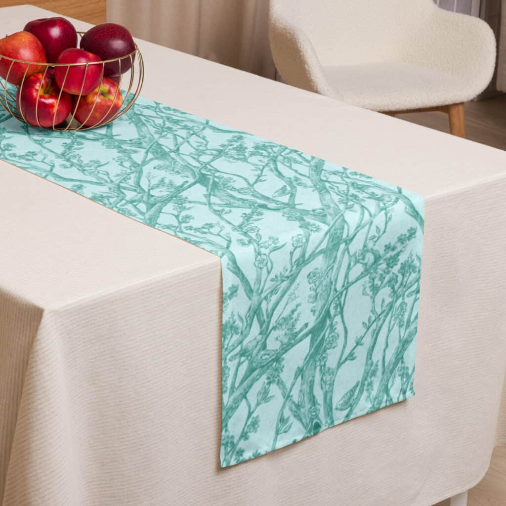 Table runner shown at edge of table, laid atop a white tablecloth.