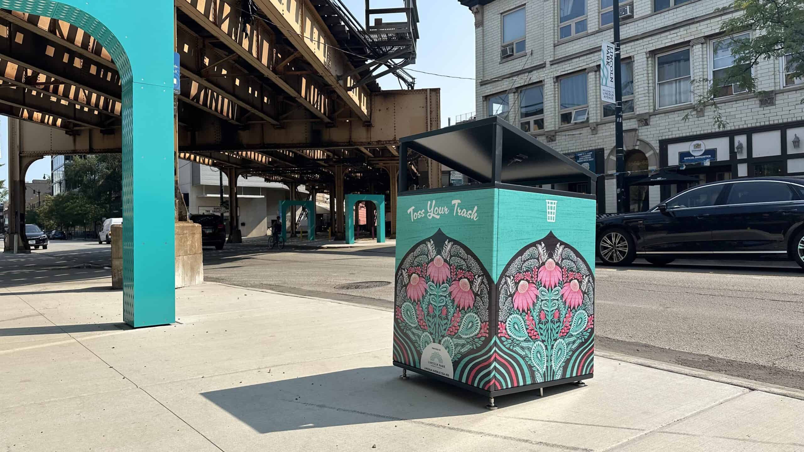 Citibin wrapped in a hand-drawn illustration of pink coneflowers and butterflies on Lincoln Avenue in Chicago, beneath the elevated train tracks.