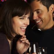 Un hombre y una mujer ríen juntos con una copa en un bar, el escenario donde encaja el método Mystery