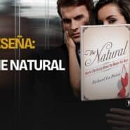 Un hombre y una mujer muy juntos en un ascensor, con el libro The Natural de Richard La Ruina en primer plano