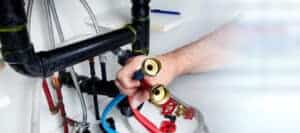 A Service Champions expert carefully holds two flexible water hoses near plumbing pipes under a sink, ready to ensure your comfort.