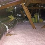 Attic with wooden beams and insulated ductwork, floor covered in pink insulation, expertly cared for by Service Champions’ PureFlow Process.