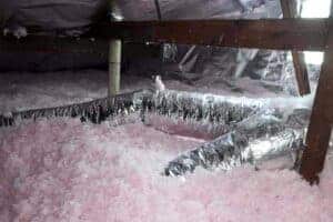 Attic featuring pink loose-fill insulation and silver HVAC ducts installed by Service Champions, ensuring comfort and trusted energy savings.