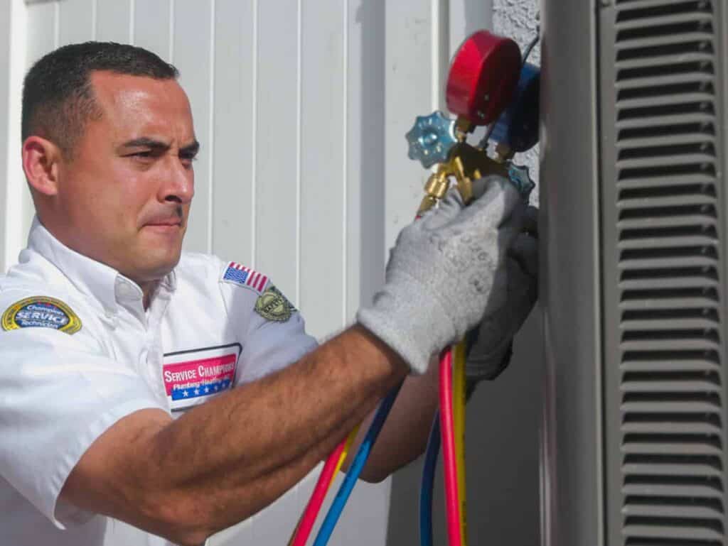 A friendly Service Champions technician services an outdoor AC unit with care, using gauges and hoses to ensure your comfort.