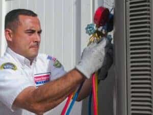A friendly Service Champions technician services an outdoor AC unit with care, using gauges and hoses to ensure your comfort.