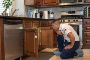 A trusted Service Champions technician inspects plumbing under a kitchen sink, ensuring comfort and peace of mind for your home.