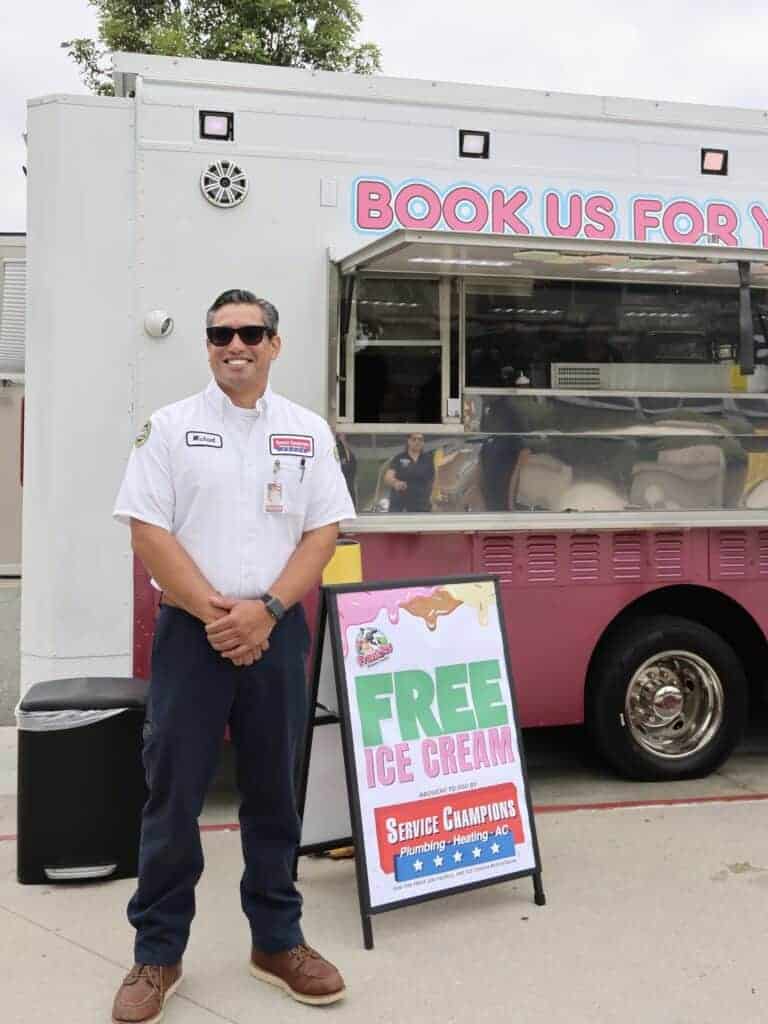 A friendly Service Champions team member in uniform stands by an ice cream truck in Anaheim, next to a sign inviting neighbors to enjoy complimentary ice cream—demonstrating the company’s commitment to helpful service and dependable home comfort as Southern California’s trusted local HVAC, plumbing, and drain experts.