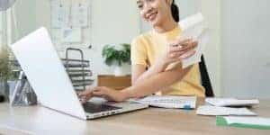 High school woman doing paperwork at desk with laptop.
