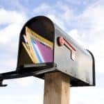 Envelope filled with direct mail marketing materials in a mailbox against a sky background.