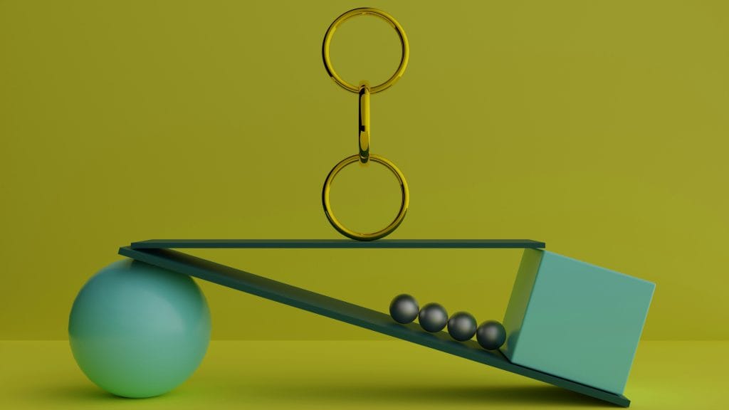 An image shows objects of different shapes balancing against one another in front of a yellow background.