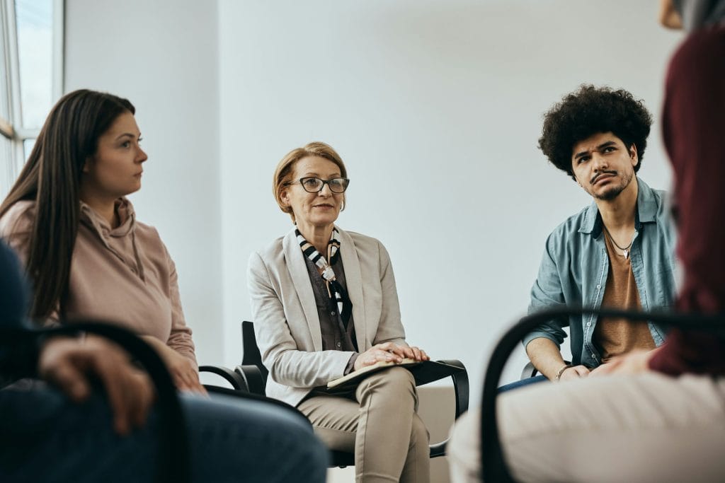 Two women and a man are pictured as part of a group, listening to others during a group discussion.