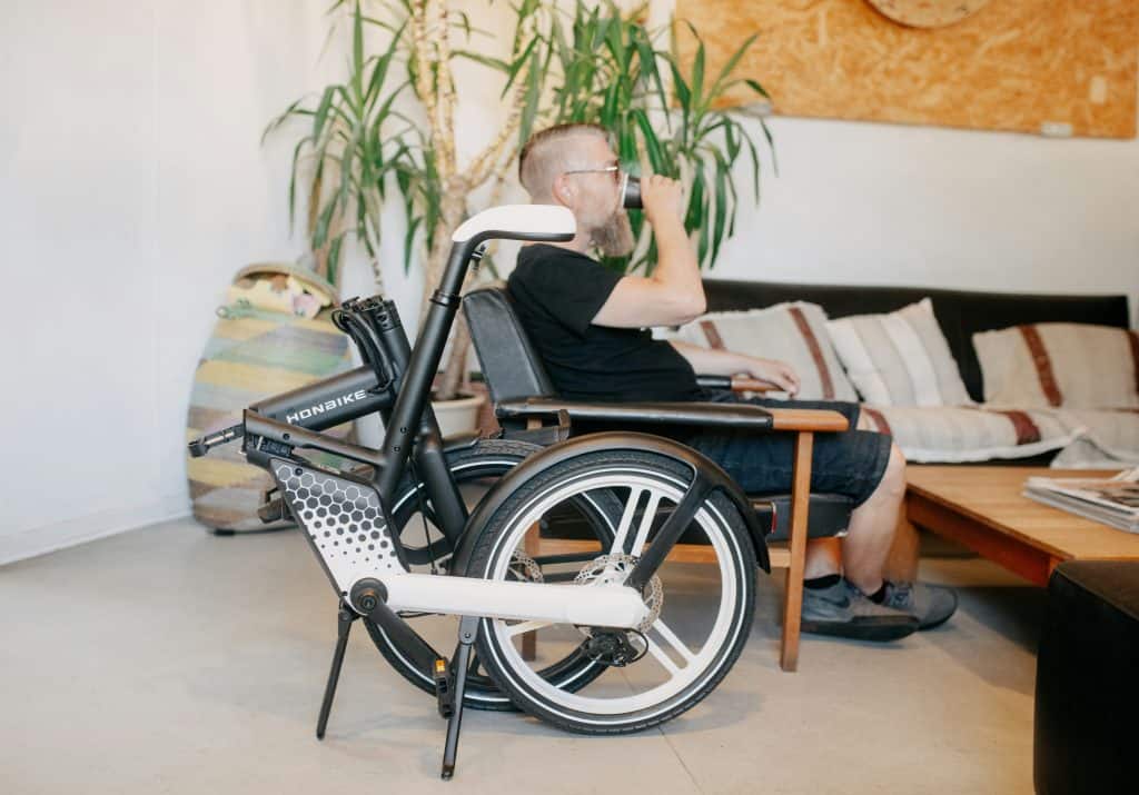 A disabled man sits in an office chair beside his wheelchair, during a therapy appointment.