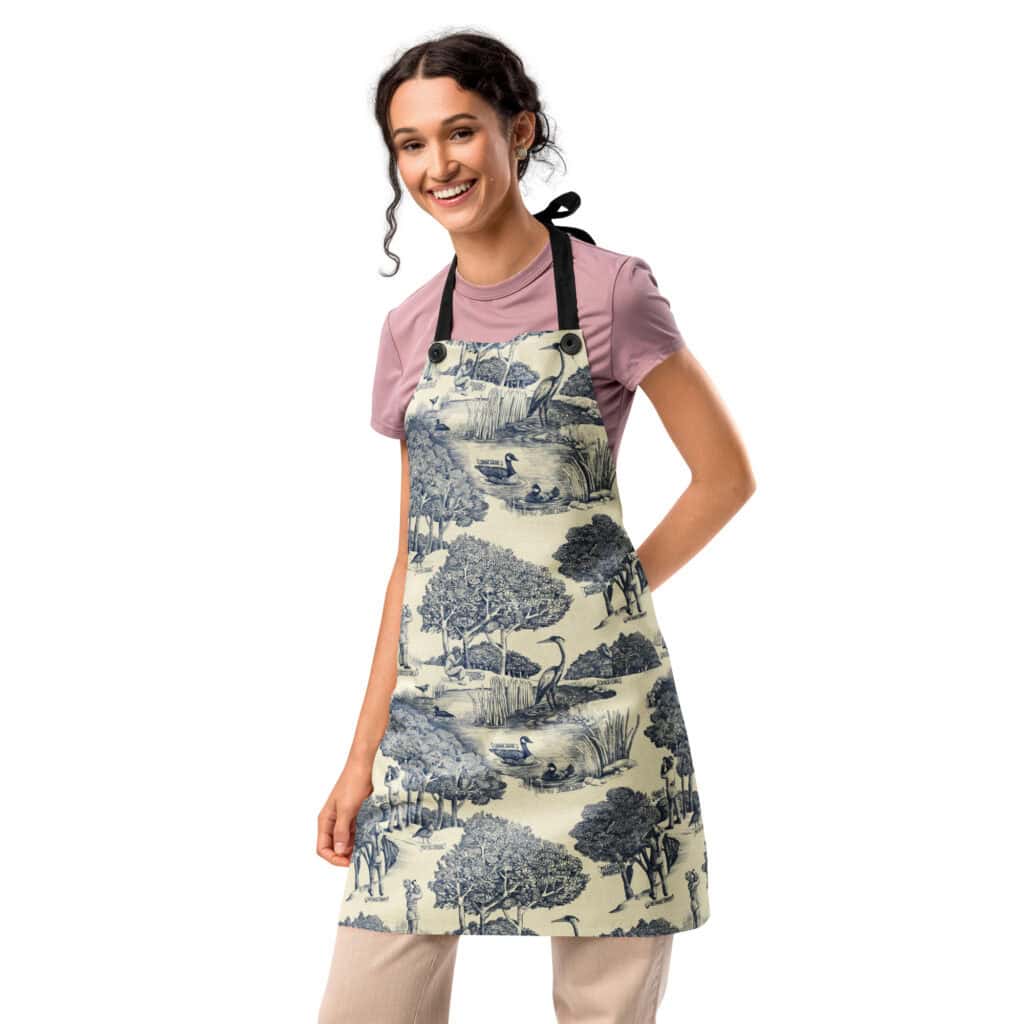 Woman wearing the Birds & Birders Toile De Jouy apron over a pink top, standing with hand on hip.
