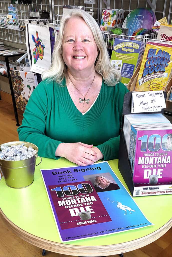 Susie Wall, author of "100 Things to do in Montana Before You Die," seated at a table at a book signing.