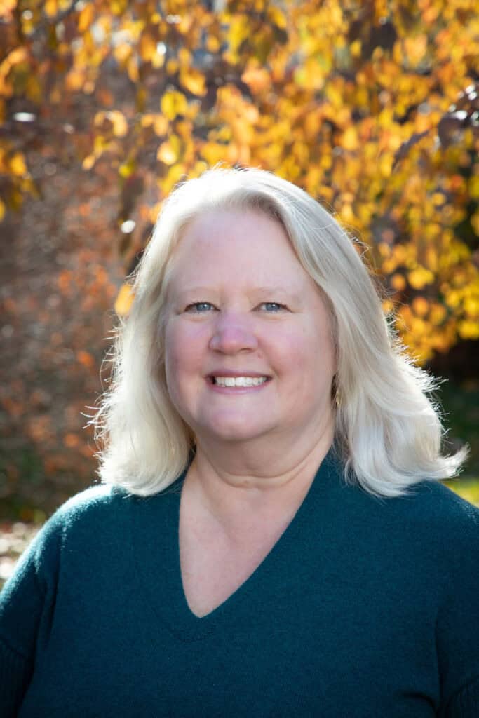 Susie Wall smiling, with fall foliage behind her.