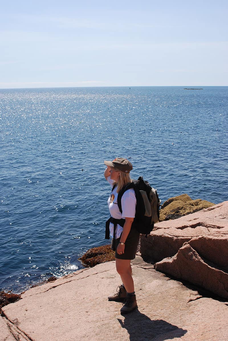 Susie Wall standing on an outcropping of rock overlooking the ocean.