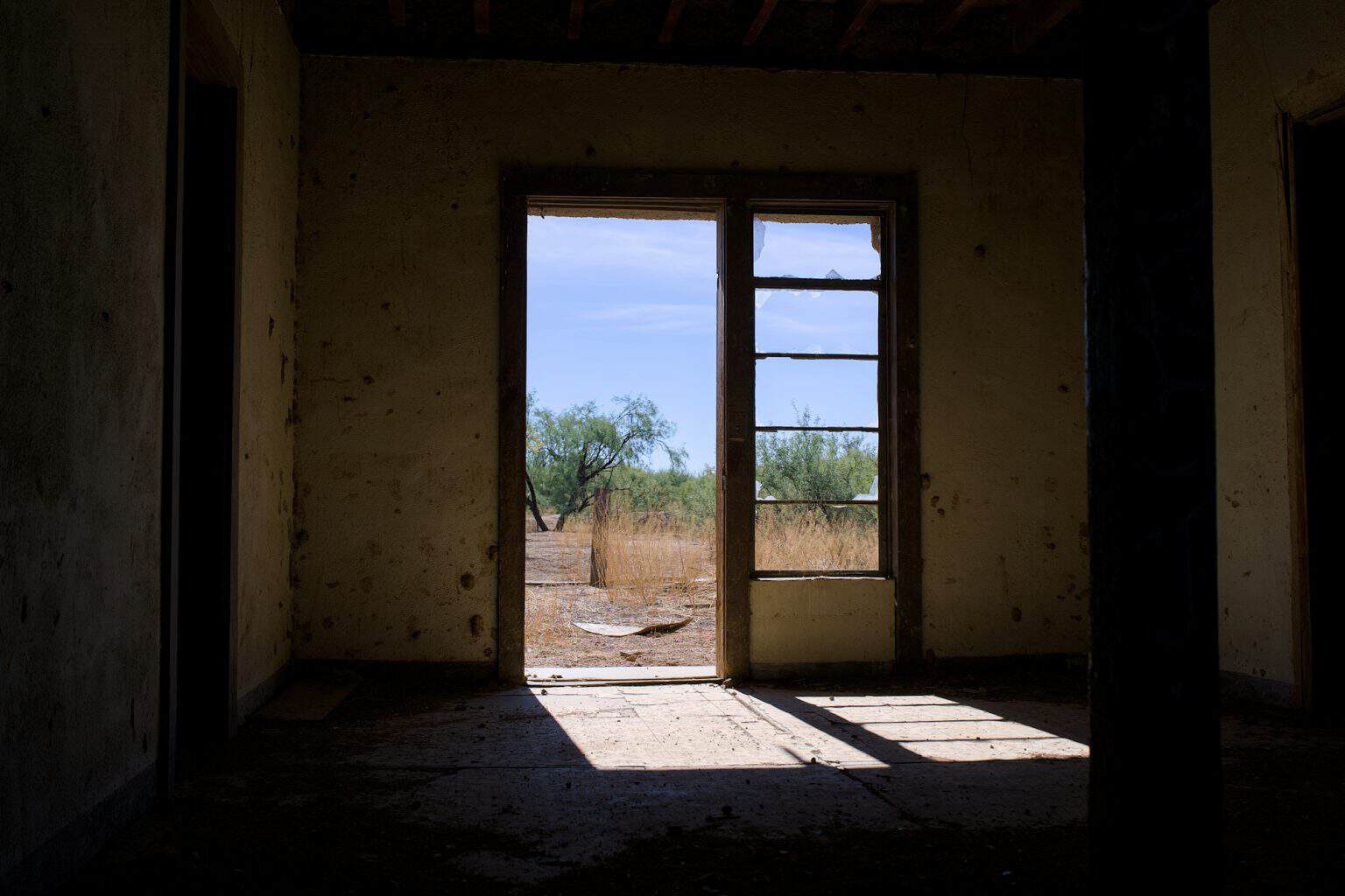 An open doorway frames a view of a sunlit, dry outdoor landscape beyond.