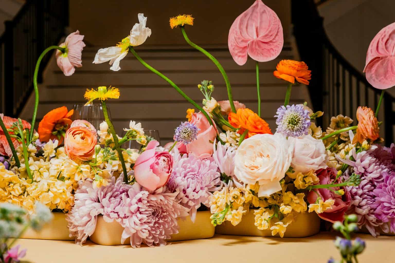 A row of vases each holding flowers of a different color, arranged side by side.