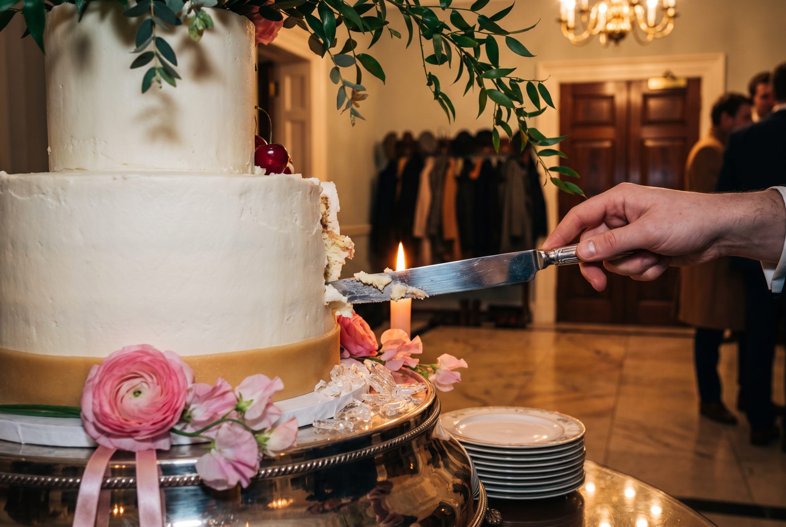 A knife cuts into the icing-white tiered cake within minutes of arrival, coats still hanging on the rack behind as guests stand in the hall.
