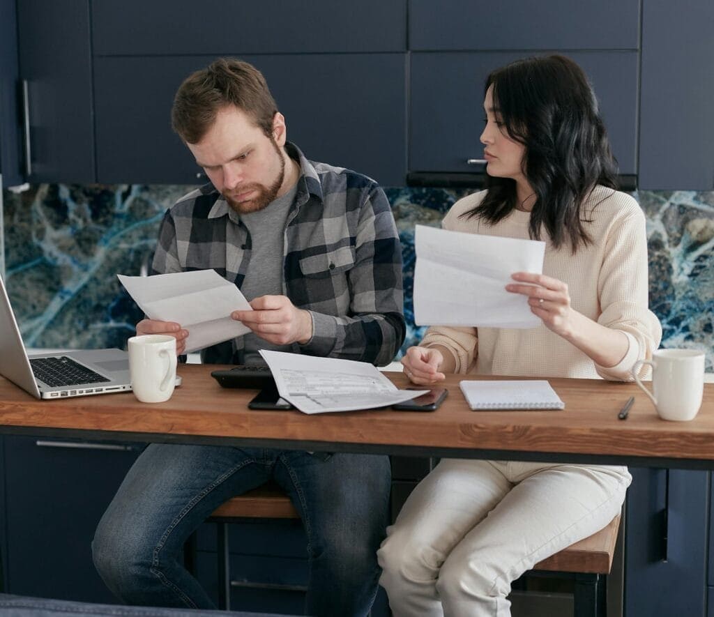 A young couple sits at home looking at financial documents with concern.