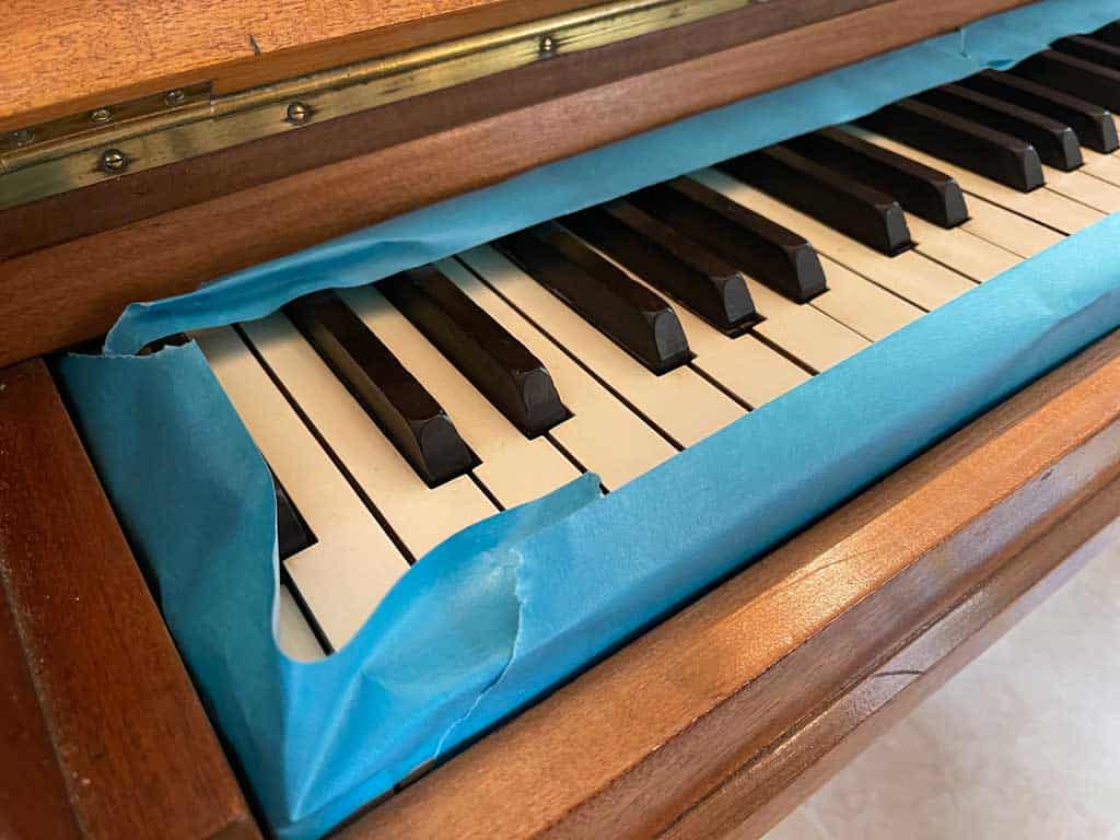 How to paint a piano: Use painter's tape to thoroughly mask off the areas that you don't want to paint. I masked the edges of the keys then covered the top with newspaper.