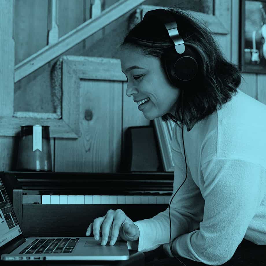 Young woman wears headphones and works at a laptop while smiling.