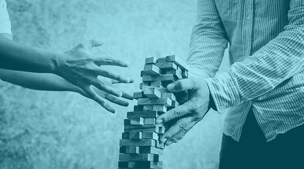 Tower of wooden Jenga blocks is falling as 2 hands try to grab it.