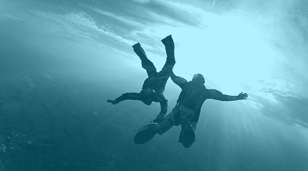 Two sky divers hold each other by the leg as they free fall