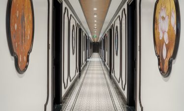 Elegant luxury cruise corridor with ornate wall art and patterned tile floor, showcasing high-end comfort.