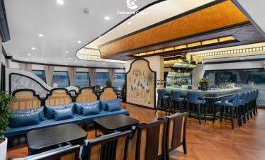 Elegant cruise lounge interior with bar, seating, and panoramic windows.
