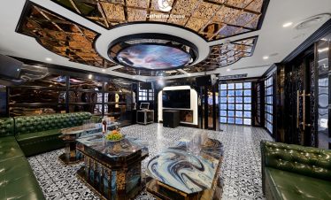 Luxurious cruise lounge with marble tables, green leather seating, and elegant interior design.