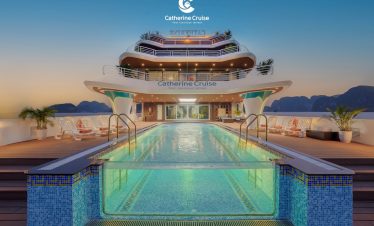 Luxury cruise ship deck with swimming pool and mountain views at sunset.
