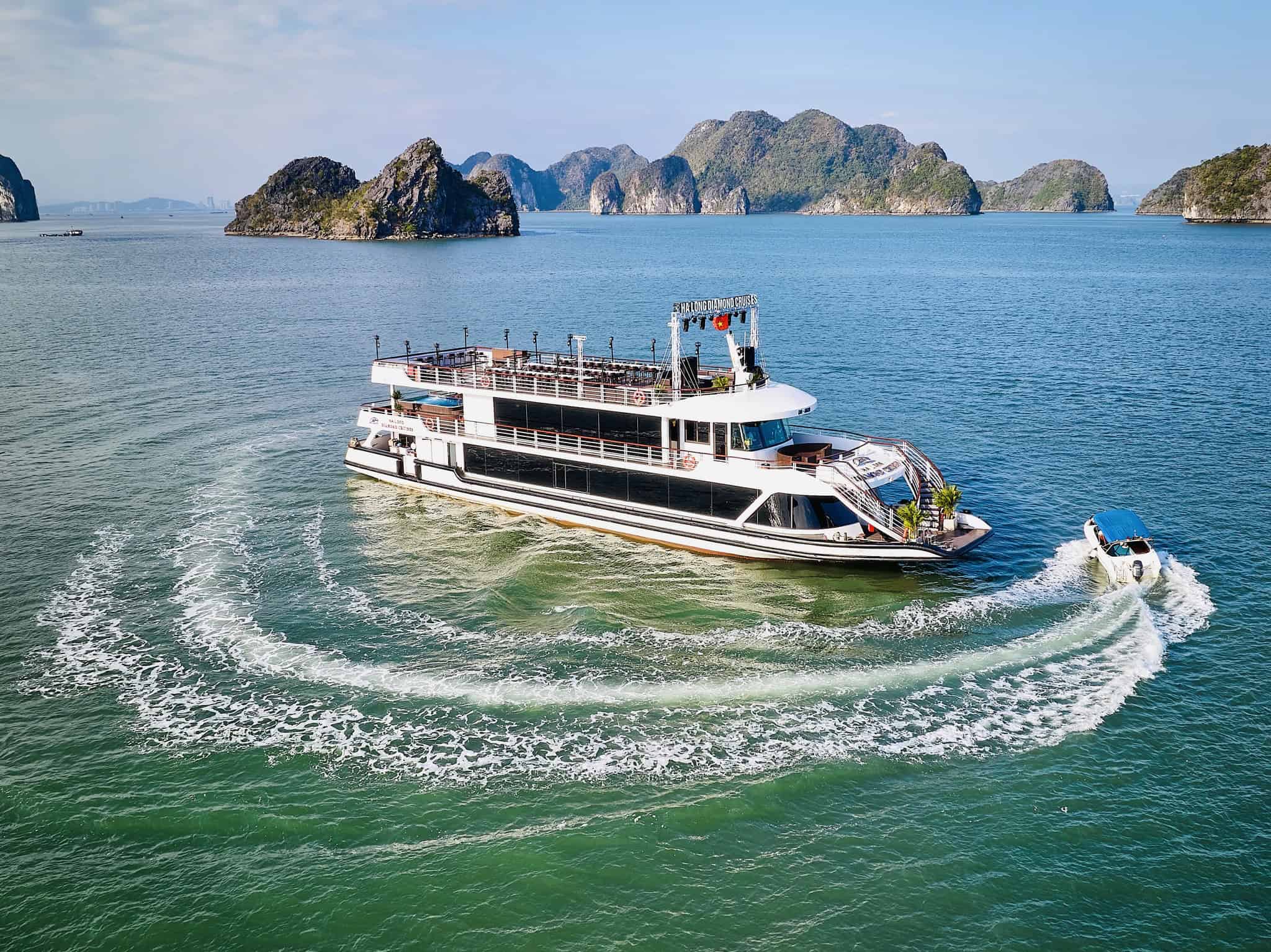 Halong Bay cruise boat sailing through emerald waters with limestone islands.