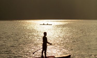 1. Person paddleboarding on a tranquil river at sunset with mountainous backdrop.