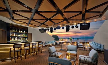 Relaxing rooftop bar with ocean view at sunset, ideal for luxury travel and tropical vacations.