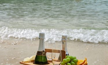Luxury beachside champagne with grapes and orange slices on sandy shore, boat in background.