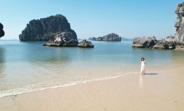 Seaside breathtaking view with rocks and clear water, woman in white dress enjoying beach scenery.