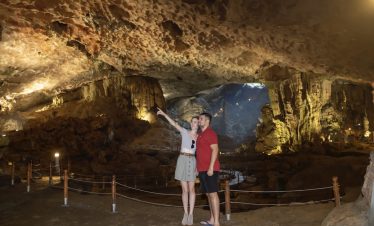 Brightly lit cave with tourists exploring underground stalactites and stalagmites in Vietnam.