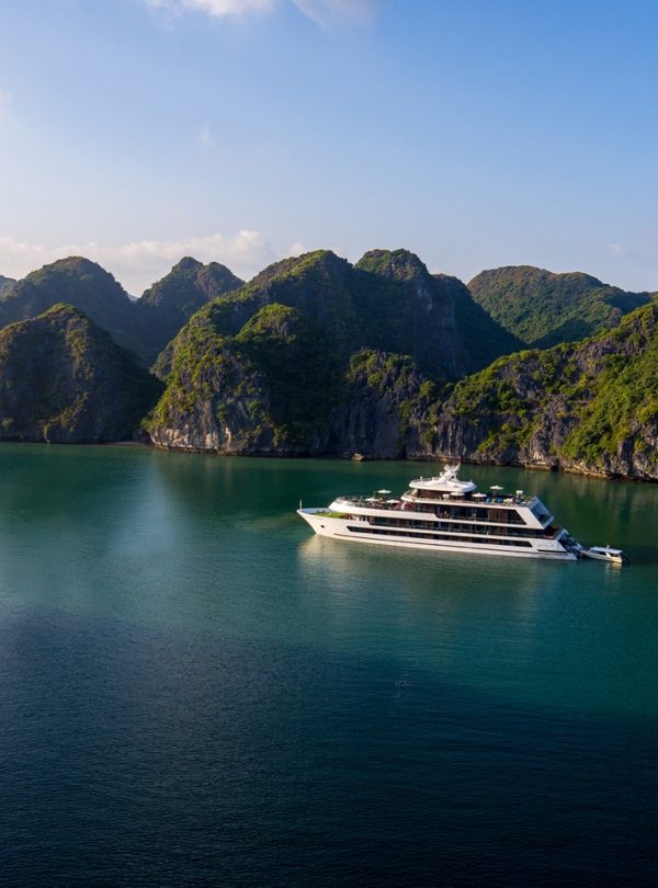 Luxurious yacht sailing through emerald waters surrounded by lush green islands in Halong Bay, Vietnam.
