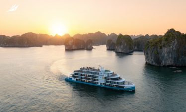 Luxurious boat cruising in Ha Long Bay during sunset with limestone islands.