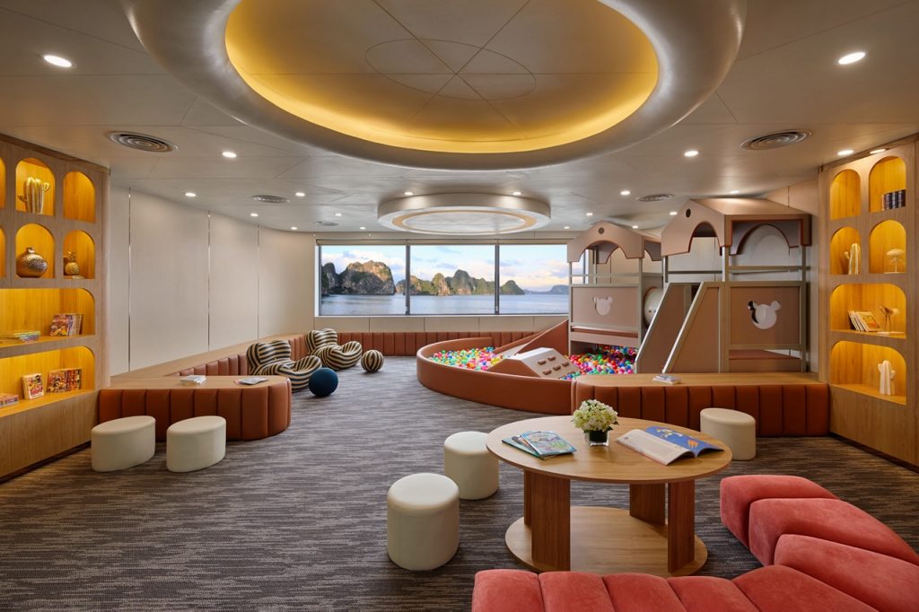 Bright indoor kids' playroom with ball pit, slides, and scenic ocean view in the background.