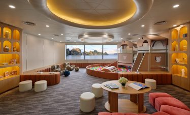 Bright indoor kids' playroom with ball pit, slides, and scenic ocean view in the background.